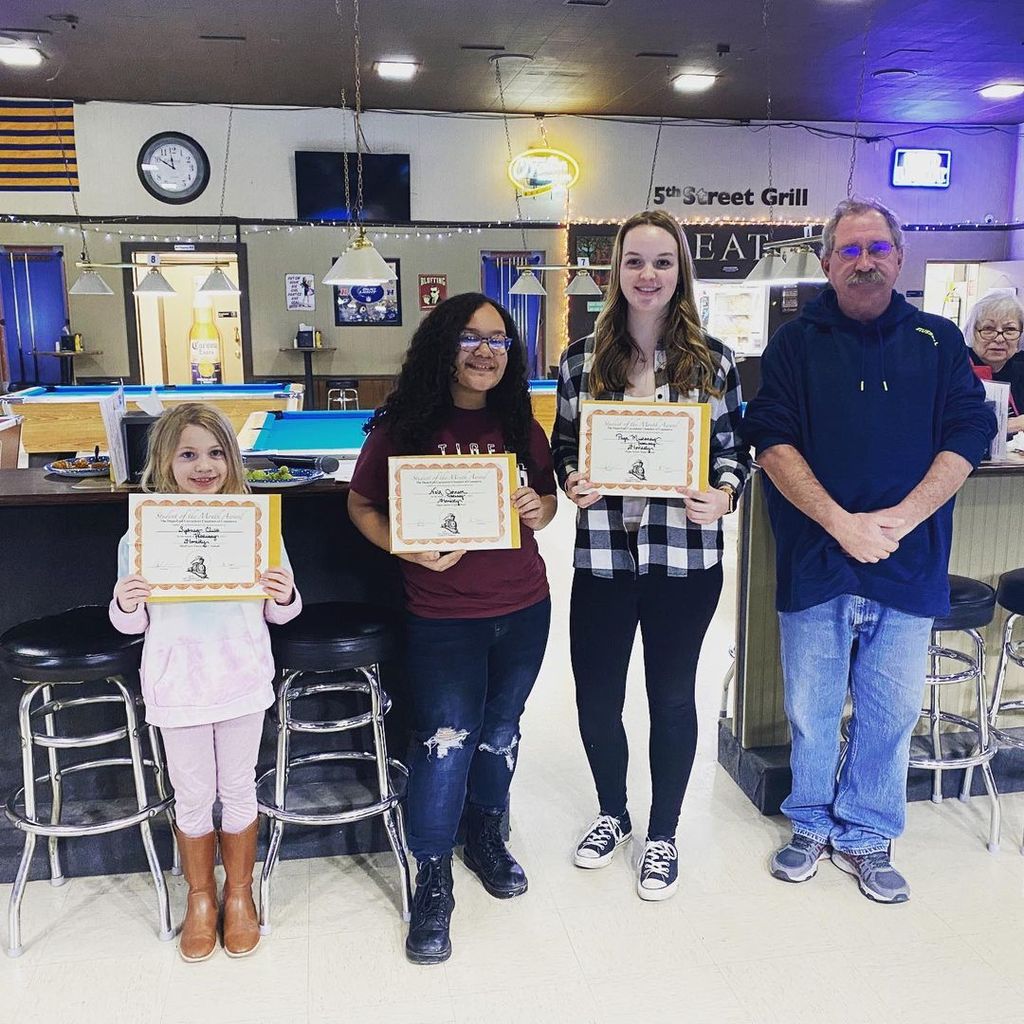3 female students holding certificates posing with a male teacher in a classroom